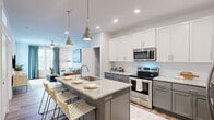 Located on Dr. Martin Luther King Jr. Blvd in New Bern, NC, this single-floor, one-bedroom, one-bathroom residence offers a thoughtfully designed layout that maximizes comfort and functionality. The open-concept kitchen is a standout feature, showcasing two-tone cabinetry with crisp white upper cabinets and soft gray lower cabinets, granite countertops, a subway tile backsplash, stainless steel appliances, and a large center island with seating — ideal for both cooking and entertaining. The kitchen flows seamlessly into the living room, which is bathed in natural light from large windows dressed with elegant draping curtains and features wood-look flooring and direct access to a private balcony. The bedroom is a serene retreat, carpeted for comfort, with multiple windows allowing abundant natural light, a ceiling fan, and a spacious walk-in closet with built-in shelving. The bathroom mirrors the kitchen's refined aesthetic with gray cabinetry and granite countertops. A dedicated in-unit laundry area with a full-size washer and dryer adds everyday convenience. Throughout the home, neutral tones and modern finishes create a clean, contemporary ambiance.