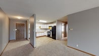 This single-floor unit is designed with a practical, open layout that connects the living area directly to the kitchen, creating a cohesive and functional common space. The living room is generously sized, finished with plush neutral carpeting, gray walls, wood-tone baseboards, and a textured ceiling. A sliding glass door with vertical blinds allows natural light to fill the space. The kitchen is well-equipped, featuring white cabinetry with wood-tone trim, ample upper and lower storage, a double sink, and black appliances including a refrigerator, electric range with overhead ventilation, and dishwasher. Tile-style flooring grounds the kitchen area. The unit includes multiple bedrooms, each carpeted and painted in a consistent neutral gray palette with wood-tone baseboards and textured ceilings. Windows fitted with blinds bring in natural light. At least one bedroom features a built-in closet with sliding wood-panel doors. The full bathroom includes a tub-shower combination, toilet, vanity with sink, a towel bar, and tile-style flooring. The overall ambiance is clean, neutral, and move-in ready, offering a straightforward and comfortable living environment.