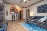 This single-floor residence offers a thoughtfully designed layout with contemporary finishes throughout. The kitchen is a standout feature, equipped with stainless steel appliances including a refrigerator, range, and microwave, complemented by rich dark cabinetry and granite-style countertops. Wood-look flooring runs through the kitchen and entry area, adding warmth and durability.

The living room is bright and welcoming, anchored by floor-to-ceiling sliding glass doors that open to a private balcony, flooding the space with natural light and providing views of the surrounding urban streetscape. Wood-look flooring continues here, and the open connection to adjacent rooms enhances the sense of flow.

The bedrooms feature plush carpeting and large windows with horizontal blinds, allowing natural light while maintaining privacy. Each room offers a comfortable, functional layout suitable for rest and study.

The bathrooms are finished with granite-topped dark vanities, large mirrors, and tiled shower-tub combinations with curved or straight curtain rods. Hexagonal wall shelving in one bathroom adds a modern decorative touch. Overall, the unit maintains a clean, contemporary aesthetic with neutral tones and modern fixtures throughout.