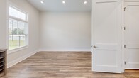 This yoga studio is a thoughtfully designed, single-floor space that prioritizes a calm, distraction-free environment for practice. The studio features warm wood-look luxury vinyl plank flooring throughout, contributing to a clean and grounded aesthetic that complements its intended use.

The main practice area is open and uncluttered, with soft neutral walls that create a serene backdrop. Multiple windows, fitted with horizontal blinds, allow natural light to filter in while offering views of an outdoor pool and surrounding greenery, enhancing the connection to nature during practice. Recessed ceiling lighting provides consistent, even illumination throughout the space.

A dedicated entryway area includes a multi-cubby shoe rack, providing organized storage for practitioners before entering the studio floor. Practical amenities such as a wall-mounted paper towel dispenser and a fire alarm system are also present. A private room with a solid-panel door offers an additional enclosed area, suitable for changing, storage, or smaller sessions.

The space is characterized by clean white baseboards, neutral paint tones, and an overall minimalist design that supports focus and relaxation. The combination of natural light, open floor space, and functional details makes this studio a well-equipped setting for yoga instruction and practice.