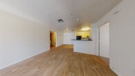 This single-floor residence offers a practical and comfortable layout across two bedrooms and two bathrooms. The open-concept living and kitchen area serves as the heart of the home, featuring warm light wood-style flooring that extends throughout the main living spaces. A sliding glass door with vertical blinds fills the living area with natural light and provides exterior access. The kitchen is defined by bold yellow cabinetry, dark countertops, and a suite of black appliances — including a full-size refrigerator, microwave, and stovetop — all anchored by a peninsula that separates the kitchen from the living area. Both bedrooms are carpeted for comfort and include ceiling fans and dedicated walk-in closets with built-in shelving and hanging rods, providing generous storage. The second bedroom features a window with blinds that brings in additional natural light. The bathrooms are finished with light wood vanities, dark countertops, large mirrors, and a shower-tub combination. A hallway connects the private areas of the home to the main living space, and the overall layout is efficient and well-organized, making practical use of the available square footage throughout.