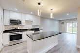 Located at 17 Kenmar Dr in Billerica, MA, this thoughtfully updated one-bedroom, one-bathroom residence offers a clean, modern aesthetic throughout its single-floor layout. The open-concept kitchen and living area serves as the heart of the home, showcasing crisp white shaker cabinetry, dark granite countertops, a subway tile backsplash, and a full suite of stainless steel appliances. A central kitchen island with a matching granite surface provides additional prep space and a natural gathering point. Elegant pendant lighting anchors the kitchen, while recessed lighting brightens the entire open area. Light wood-look flooring flows seamlessly throughout, creating a cohesive and airy feel. The living area is bathed in natural light from a sliding glass door that opens to a private balcony with outdoor views. The bedroom is a well-proportioned, quiet retreat featuring a window with natural light, recessed lighting, and baseboard heating. The bathroom is finished with wood-look tile flooring, a white vanity, and a tub-shower combination accented by striking marble-style wall tile. A hallway connects the rooms efficiently, completing this well-appointed and move-in-ready residence.