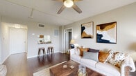 Located at 1200 South Courtenay Parkway on Merritt Island, Florida, this two-bedroom, two-bathroom residence offers a thoughtfully designed single-level layout with a comfortable and cohesive feel throughout. Rich wood-style flooring runs through the main living areas, complemented by neutral-toned walls and textured ceilings, creating a warm and inviting ambiance.

The living room is generously proportioned, featuring a ceiling fan and large sliding glass doors that open to a private balcony, flooding the space with natural light and providing open outdoor views. A pass-through kitchen with granite-style countertops and warm cabinetry overlooks the main living area, with bar seating adding a convenient casual dining option.

The spacious primary bedroom is appointed with plush carpeting, a ceiling fan, and ample natural light from wide windows dressed in sheer curtains. It is accompanied by a well-sized walk-in closet with wire shelving. The second bedroom, also carpeted and ceiling fan-equipped, offers versatility as a home office or guest room.

Both bathrooms are finished with warm wood cabinetry and granite-look countertops. The full bath includes a tub-shower combination with tile surround and mosaic tile flooring. Additional features include a utility room, a second walk-in closet with wood-style flooring, and a hallway connecting all rooms efficiently.