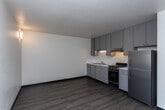 Located in Boise, Idaho, this single-floor 1-bedroom unit offers a practical and straightforward layout designed for comfortable everyday living. The main living area features light wood-style laminate flooring and neutral white walls, creating a bright, clean atmosphere. A wall-mounted light fixture adds a warm accent, while a window allows natural light to flow into the space. One room showcases a distinctive cinder block accent wall painted in a soft cream tone, adding a touch of industrial character, complemented by the same durable laminate flooring. The kitchen is efficiently designed with upper and lower cabinetry in a two-tone gray and light blue palette, offering ample storage. It is equipped with an electric range, an overhead ventilation hood, a double-basin sink, and a full-size refrigerator. The bedroom is carpeted for added comfort and includes an impressive built-in storage wall featuring a wide closet with a hanging rod and a tall shelving unit beside it, providing substantial organizational space. An adjacent door leads directly to the bathroom, which includes a shower-tub combination. Additional built-in shelving near the entryway offers further storage convenience. Overall, the unit presents a functional, no-frills living space with practical storage solutions throughout.