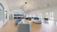 Located at 3701 Grapevine Mills Pkwy in Grapevine, TX, this single-story community facility spans a generous footprint across seven thoughtfully designed areas. The centerpiece is a grand open lounge defined by soaring vaulted ceilings, rich hardwood-style flooring, and an eye-catching triple-ring modern chandelier. Walls of large French doors and multi-pane windows flood the space with natural light while framing outdoor views. Elegant arched entryways connect the lounge to adjacent areas, lending a refined architectural character throughout. Seating arrangements with navy and neutral upholstered furniture create inviting gathering zones, complemented by a built-in kitchenette area with teal cabinetry, stone countertops, and stainless steel appliances. A dedicated fitness center offers a full suite of cardio and strength training equipment across two rooms with patterned carpet flooring and wall-mounted mirrors. Private office workspaces feature patterned carpet, arched windows, and individual desks suited for focused work. A conference/dining area showcases herringbone-patterned tile flooring, marble-top tables, blue upholstered chairs, and a wall-mounted display screen. An entry foyer with arched alcoves, sconce lighting, and warm hardwood floors completes the welcoming atmosphere of this well-appointed facility.
