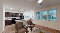 This thoughtfully designed 2-bedroom, 2-bathroom model home in Clermont, Florida offers a well-appointed single-floor layout that balances comfort and functionality. The open-concept living area features warm wood-look flooring, neutral walls, and multiple windows that flood the space with natural light and offer views of the lush outdoor surroundings. A ceiling fan and contemporary pendant lighting add to the inviting ambiance.

The kitchen is outfitted with rich dark cabinetry, granite countertops, black appliances, and a peninsula that provides additional prep and seating space. Just beyond, a sun-drenched dining nook is wrapped in windows on two sides, creating a bright and airy setting for everyday meals.

Both bedrooms are generously sized with plush carpeting and ample natural light. The primary bedroom connects to a well-sized bathroom featuring a dual-sink vanity with granite countertops, dark cabinetry, wood-look flooring, and a tub-shower combination. A spacious walk-in closet with wire shelving provides abundant storage.

A dedicated laundry area is conveniently accessible from the kitchen, adding everyday practicality. Throughout the home, consistent finishes and a clean, neutral palette create a cohesive and welcoming atmosphere suited to a variety of lifestyles.