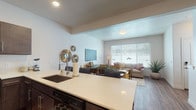 This thoughtfully designed two-floor residence offers a seamless blend of comfort and modern style. The main level opens into a bright, open-concept layout where the kitchen flows effortlessly into the dining and living areas. The kitchen is outfitted with dark espresso cabinetry, light quartz countertops, a deep undermount sink, and a full suite of black appliances including a range, microwave, dishwasher, and a side-by-side refrigerator. A generous island provides additional workspace and casual seating.

The living room is anchored by a large picture window that fills the space with natural light, complementing the warm wood-look flooring found throughout the main level. Upstairs, the primary bedroom is a spacious retreat featuring plush carpet, direct access to a walk-in closet with built-in shelving and hanging rods, and a private en-suite bathroom. The en-suite features dark cabinetry with quartz countertops, wood-look flooring, and a shower-tub combination. A secondary bedroom offers multiple windows and comfortable carpeting, served by an additional full bathroom with consistent finishes. Clean white walls, recessed lighting, and panel doors complete the polished, contemporary aesthetic throughout.
