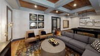 Located at 1717 E Belt Line Rd in Coppell, Texas, this single-floor amenity space offers a sophisticated and well-appointed environment designed for both relaxation and productivity. The interior is anchored by a striking coffered ceiling with warm wood-paneled inlays and recessed lighting, lending a refined yet inviting character throughout.

The main lounge area features a generously sized sectional sofa arrangement centered around a round concrete coffee table, all set atop a richly patterned area rug with earthy gold, blue, and brown tones. A wall-mounted flat-screen TV and coordinating media console complete the space for comfortable gathering. Adjacent to the lounge, a game room area includes additional seating — leather accent chairs alongside a sofa — a pool table, and curated wall art including decorative circular mirrors and a framed game board.

A café-style nook provides intimate seating with bistro tables and a cushioned bench set against a bold textured feature wall, ideal for casual conversation or quiet moments. Rustic wood flooring ties each area together seamlessly.

The business center offers a curved wraparound workstation with multiple computer stations, a printer, and natural window light — all accented by warm-toned walls and a large abstract painting. Throughout the space, thoughtful decorative touches, cohesive furnishings, and layered lighting create an upscale, community-focused atmosphere.