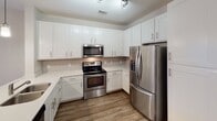 Located at 151 E Blount Ave in Knoxville, Tennessee, this single-floor unit offers a thoughtfully designed open-concept layout that seamlessly connects the kitchen and living area. The kitchen is a standout feature, outfitted with crisp white shaker-style cabinetry, light quartz countertops, a subway tile backsplash, and a full suite of stainless steel appliances including a French door refrigerator, electric range, built-in microwave, and dishwasher. A central island with a sink and pendant lighting adds both functionality and style. Wood-look plank flooring runs throughout the main living areas, complementing the neutral color palette and contributing to a clean, contemporary aesthetic. The living area is bathed in natural light from double doors that open to an outdoor view, and a ceiling fan adds comfort to the space. The bedrooms are carpeted for warmth and comfort, each equipped with a ceiling fan and ample natural light from windows with blinds. One bedroom features a walk-in closet, providing generous storage. The bathroom is finished with light wood-look tile flooring, white subway tile surrounding the tub-shower combination, and clean white fixtures throughout, creating a bright and airy feel. The overall design is modern, cohesive, and move-in ready.
