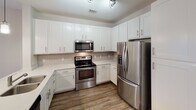 Located at 151 E Blount Ave in Knoxville, Tennessee, this single-floor unit offers a thoughtfully designed open-concept layout that seamlessly connects the kitchen and living area. The kitchen is a standout feature, outfitted with crisp white shaker-style cabinetry, light quartz countertops, a subway tile backsplash, and a full suite of stainless steel appliances including a French door refrigerator, electric range, built-in microwave, and dishwasher. A central island with a sink and pendant lighting adds both functionality and style. Wood-look plank flooring runs throughout the main living areas, complementing the neutral color palette and contributing to a clean, contemporary aesthetic. The living area is bathed in natural light from double doors that open to an outdoor view, and a ceiling fan adds comfort to the space. The bedrooms are carpeted for warmth and comfort, each equipped with a ceiling fan and ample natural light from windows with blinds. One bedroom features a walk-in closet, providing generous storage. The bathroom is finished with light wood-look tile flooring, white subway tile surrounding the tub-shower combination, and clean white fixtures throughout, creating a bright and airy feel. The overall design is modern, cohesive, and move-in ready.