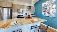 Located at 315 Edith Ave in Nashville, Tennessee, Unit 308 is a thoughtfully designed single-floor residence that blends contemporary style with everyday functionality. The open-concept kitchen serves as a visual centerpiece, featuring granite countertops, a spacious island with bar seating, gray cabinetry, stainless steel appliances including a range and built-in microwave, subway tile backsplash, and wood-look flooring. A bold teal accent wall adds a striking pop of color, complemented by modern pendant lighting overhead.

The living area offers a welcoming atmosphere with natural light streaming through a large window dressed in warm, sheer curtains. Wood-look flooring continues through this space, which also includes a dedicated nook with a sleek wall-mounted shelving unit and a comfortable accent chair — ideal as a reading or work area.

The bedroom is carpeted and generously sized, with windows providing ample natural light, a ceiling fan, and convenient access to both the walk-in closet and in-unit laundry. The walk-in closet features wire shelving for flexible storage. The bathroom is clean and bright, finished with white tile and a glass-enclosed standing shower with brushed nickel fixtures. Throughout, the unit maintains a cohesive, modern aesthetic with neutral tones and quality finishes.