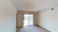This single-story unit offers a practical and straightforward layout across several well-defined spaces. The main living area is generously sized, featuring neutral-toned carpet underfoot, smooth white walls, and a textured ceiling. A large sliding glass door floods the room with natural light and provides direct access to an outdoor balcony, framing views of surrounding greenery. Vertical blinds offer flexible light control throughout the day.

The kitchen is efficiently laid out with wood-look flooring, white upper and lower cabinetry, light countertops, and a full suite of white appliances including a refrigerator, electric range, and dishwasher. A utility panel is conveniently located just off the kitchen entry.

The bedrooms are carpeted and well-proportioned, each featuring sliding wood-paneled closet doors with built-in rod and shelf storage. One bedroom includes direct access to the bathroom, which is equipped with a single-sink vanity, mirrored medicine cabinets with lighted fixtures, a toilet, and a tiled shower-tub combination. Additional rooms provide flexible use as secondary bedrooms or office space, each with natural light from windows fitted with horizontal blinds.