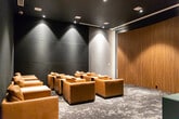 Located at 40 Lagerfeld Dr in Brampton, Ontario, this private screening room is designed to deliver an immersive, cinema-quality experience in a refined and intimate setting. The room is defined by its sophisticated dark aesthetic, with deep charcoal and near-black walls that create a focused, theatre-like atmosphere enhanced by strategically placed recessed spotlights that cast warm, dramatic washes of light across the space.

The seating arrangement features multiple rows of generously sized tan leather armchairs and sofas, each paired with small side tables for added convenience — offering a comfortable and luxurious viewing experience. The flooring is a bold, abstract-patterned carpet in dark grey and white tones, adding visual texture that complements the room's moody ambiance.

A standout feature is the rich wood-panelled accent wall, which introduces a warm, natural contrast to the otherwise dark interior palette. At the back of the room, a console table and a classic red popcorn machine add a playful, authentic cinema touch. A digital podium or control panel near the entrance provides seamless management of the room's functions. The dark ceiling with recessed lighting reinforces the immersive, purpose-built nature of this thoughtfully designed screening space.