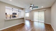 Located in Austin's desirable 78704 zip code, this 1-bedroom, 1-bathroom unit offers a thoughtfully designed layout that maximizes every inch of its comfortable footprint. The open-concept living and kitchen area serves as the heart of the home, where rich hardwood-style flooring runs throughout, reflecting natural light that pours in through a full-width sliding glass door. The door opens to an outdoor view framed by lush greenery, while vertical blinds provide privacy and light control. A ceiling fan with integrated lighting completes the airy living space. The kitchen is a standout feature, boasting crisp white cabinetry, granite-style countertops, stainless steel appliances including a range, microwave, and refrigerator, and a striking chevron-patterned tile backsplash. A peninsula counter with pendant lighting creates a natural divide between the kitchen and living area. The bedroom offers plush carpeting, a ceiling fan, natural light from a window with blinds, and a full-width closet with modern sliding mirrored panel doors. The bathroom is clean and contemporary, featuring white subway tile surrounding the tub-shower combo, white cabinetry with matte black hardware, a granite-topped vanity, and hardwood-style flooring. Neutral tones throughout create a cohesive, move-in-ready atmosphere.