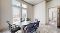 This well-appointed office suite is organized across a single floor and comprises three distinct functional areas designed to support focused work and collaborative meetings. The conference room serves as a central gathering space, featuring an oval table surrounded by ergonomic mesh chairs and bathed in natural light from large, multi-pane windows fitted with horizontal blinds. Soaring ceiling heights amplify the sense of openness and airiness in this room, giving it a professional yet welcoming atmosphere.

Adjacent to the conference room is a dedicated workstation area outfitted with built-in light wood cabinetry and desks arranged along the perimeter walls. Multiple workstations with ergonomic seating provide ample room for individual productivity. Floor-to-ceiling windows flood this space with natural light, while framed landscape artwork adds a refined touch to the neutral, warm-toned walls. Patterned carpet throughout provides texture underfoot and contributes to the space's quiet, focused environment.

A smaller secondary meeting room rounds out the suite, offering a more intimate setting for private conversations or focused sessions, with its own table, seating, and framed wall art. Frosted glass panel doors connect the spaces while maintaining visual privacy. The consistent use of neutral beige tones, recessed lighting, and quality finishes throughout creates a cohesive, polished professional environment.