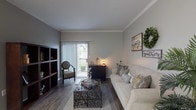 This single-floor 2-bedroom, 1-bathroom residence offers a thoughtfully designed layout with consistent wood-style flooring throughout the main living areas. The living room is a welcoming space accented by elegant crown molding, neutral gray walls, and dark hardwood-style floors. A sliding glass door floods the room with natural light while providing direct access to an outdoor patio. The kitchen is efficiently laid out in a galley style, featuring white cabinetry, gray countertops, a tile backsplash, and white appliances, including a range, refrigerator, and dishwasher. A peninsula counter separates the kitchen from the adjacent dining area, creating a natural flow between spaces. Both bedrooms are carpeted and comfortably sized, with the primary bedroom offering a mirrored sliding closet and windows that frame outdoor views. The full bathroom is clean and functional, finished with wood-style flooring, a tiled shower-tub combination, and overhead storage. The overall ambiance of the home is warm and inviting, combining practical design with comfortable finishes throughout.