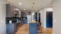 Located at 299 Debaliviere Ave in St. Louis, Missouri, this thoughtfully designed unit on a single floor offers a seamless blend of modern aesthetics and functional living. The open-concept layout connects the kitchen and living area, creating an inviting, cohesive space bathed in natural light from large, black-framed windows.

The kitchen is a standout feature, showcasing rich dark-toned shaker-style cabinetry, dark countertops, and a teal-toned tile backsplash that adds a distinctive pop of color. A full suite of stainless steel appliances — including a refrigerator, range, microwave, and dishwasher — provides modern convenience. A central island with a dark stone countertop offers additional prep space and casual seating, illuminated by elegant pendant lights with glass shades.

Light wood-tone flooring flows throughout the unit, lending warmth and continuity. The living area is generously proportioned, with large windows framing views of the surrounding St. Louis neighborhood and allowing natural light to fill the room.

The bedroom is a serene retreat, featuring a large window with an outdoor neighborhood view and ample natural light. The bathroom is well-appointed with a dual-sink vanity, clean white countertops, dark wood cabinetry, and a frosted-glass door for added privacy. Overall, the space delivers a polished, contemporary feel throughout.