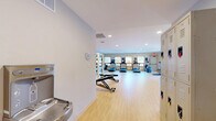 The fitness center at 1570 Eustis St in Lauderdale, Minnesota, offers a spacious, single-floor exercise room designed to support a comprehensive workout experience. The space features light hardwood-style flooring throughout, recessed ceiling lighting, and neutral white and gray walls that create a clean, energizing atmosphere.

The cardio area is well-appointed with multiple treadmills, elliptical trainers, a stationary bike, and a rowing machine, all positioned near a row of wood-trimmed windows that invite natural light and provide views of the surrounding greenery. This layout ensures a bright and motivating environment for endurance training.

The strength training section is equally well-equipped, featuring a multi-station cable machine, a full dumbbell rack ranging across multiple weight increments, kettlebells, and an adjustable workout bench. A large wall mirror spans the strength area, enhancing the sense of openness and allowing for proper form checks during exercise.

Additional details include built-in shelving, a water station near the entrance, and lockers for personal storage. The open floor plan provides ample room to move freely between equipment zones. The overall design balances functionality with a welcoming ambiance, making this fitness center a practical and well-organized facility for residents and users alike.