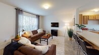 Located in the Oak Hill Townhomes community in State College, PA, this three-floor townhome offers a practical and comfortable layout suited for everyday living. The main living area features a carpeted floor, neutral walls, and a large window that fills the space with natural light, complemented by seating and a wall-mounted television. The kitchen and dining area is outfitted with warm oak cabinetry, white appliances including a dishwasher, stove, and refrigerator, and a large window overlooking the outdoors, creating a bright and inviting space for meals. A dining table with wooden chairs sits centrally on tile flooring, adding to the functional charm. Multiple bedrooms are spread across the floors, each carpeted and featuring windows with blinds and curtains for privacy and light control. The bedrooms offer ample space for sleeping and studying, with room for a desk and additional furnishings. Bathrooms include vanities with wooden cabinetry, white countertops, and a mix of shower-tub combinations and standalone shower stalls with classic tile flooring. A utility area on the lower level houses the water heater and network infrastructure, tucked efficiently beneath the staircase. The townhome's clean, neutral palette and consistent finishes create a cohesive and livable atmosphere throughout.