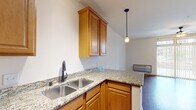 This single-floor unit offers a practical and cohesive layout centered around an open-concept kitchen and living area. The kitchen is well-appointed with warm honey-toned wood cabinetry, granite countertops, a double stainless steel sink, and black appliances including a range, over-the-range microwave, and dishwasher. A peninsula counter separates the kitchen from the living space, providing additional prep area and an open sightline throughout. Pendant lighting above the peninsula adds a functional decorative touch, complemented by track lighting near the entry.

Hardwood-style flooring runs consistently throughout the main living areas, lending warmth and visual continuity. The living area is spacious and bright, anchored by a ceiling fan and a large sliding glass door that invites natural light and provides outdoor access. Vertical blinds offer privacy and light control.

An additional room features the same flooring and neutral walls, offering flexible use as a bedroom or office. A dedicated closet with a built-in rack provides convenient storage near the entry.

The bathroom includes a wood-toned vanity with an integrated sink, a large mirror with vanity lighting, a toilet, and a shower-tub combination, all finished with the same warm hardwood-style flooring that unifies the overall aesthetic of the space.