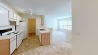 Located at 2350 Carlyle Place Dr in Winston-Salem, NC, this single-floor residence offers a well-organized layout designed for comfortable everyday living. The galley-style kitchen is efficiently arranged with light wood cabinetry on both sides, white appliances including a range and refrigerator, tile flooring, and track lighting overhead. A peninsula with a built-in sink provides a natural transition into the open living area, which features soft wall-to-wall carpeting and large windows that invite generous natural light and views of surrounding greenery. The bedrooms continue the warm, neutral palette with plush carpeting, bright windows framing outdoor views, and ample closet storage, including a double-door closet in one room. The bathroom is clean and functional, featuring a full tub and shower combination with chrome fixtures, complemented by crisp white walls and a simple, understated design. Throughout the residence, the light color scheme of warm whites and beiges creates a cohesive, calm atmosphere. The floor plan, visible in the dollhouse view, reveals a logical and accessible single-level arrangement with well-defined spaces that flow naturally from one area to the next.