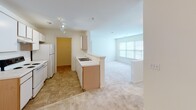 Located at 2350 Carlyle Place Dr in Winston-Salem, NC, this single-floor residence offers a well-organized layout designed for comfortable everyday living. The galley-style kitchen is efficiently arranged with light wood cabinetry on both sides, white appliances including a range and refrigerator, tile flooring, and track lighting overhead. A peninsula with a built-in sink provides a natural transition into the open living area, which features soft wall-to-wall carpeting and large windows that invite generous natural light and views of surrounding greenery. The bedrooms continue the warm, neutral palette with plush carpeting, bright windows framing outdoor views, and ample closet storage, including a double-door closet in one room. The bathroom is clean and functional, featuring a full tub and shower combination with chrome fixtures, complemented by crisp white walls and a simple, understated design. Throughout the residence, the light color scheme of warm whites and beiges creates a cohesive, calm atmosphere. The floor plan, visible in the dollhouse view, reveals a logical and accessible single-level arrangement with well-defined spaces that flow naturally from one area to the next.