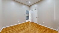 Located at 81 Academy St in Poughkeepsie, NY, this single-floor, two-bedroom, one-bathroom unit offers a compact yet efficiently arranged layout with thoughtful finishes throughout. The kitchen serves as a standout feature, showcasing gray shaker-style cabinetry, quartz countertops, a subway tile backsplash, a stainless steel sink, and gleaming large-format white tile flooring. A built-in counter with bar seating adds a functional dining element to this well-appointed galley-style space. Recessed lighting and a view toward the entry door give the kitchen an open, welcoming feel. Both bedrooms are finished with warm hardwood flooring and neutral gray walls, creating a calm and versatile atmosphere. The primary bedroom offers a closet and natural light from a window dressed with decorative curtains, while a baseboard heating unit ensures year-round comfort. The second bedroom provides direct sightlines to the kitchen and features recessed lighting. The bathroom is cleanly finished with wood-look tile flooring, a tub and shower combination with marble-style surround, a pedestal sink, and a floral shower curtain that adds a touch of character. White panel doors and bright white trim are consistent throughout, tying the space together with a crisp, cohesive aesthetic.