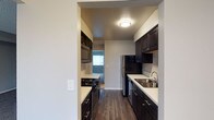 This single-floor residence offers a thoughtfully designed layout centered around a sleek galley-style kitchen. The kitchen is outfitted with rich, dark espresso cabinetry that extends from floor to ceiling on both sides, providing ample storage throughout. Light-toned countertops create a striking contrast against the dark cabinets, adding visual depth to the space. Stainless steel appliances — including a refrigerator, dishwasher, and built-in microwave — are complemented by a gas range cooktop, making the kitchen both functional and stylish. A stainless steel undermount sink with a modern faucet is conveniently positioned along the countertop. The kitchen is finished with warm wood-look flooring that runs continuously underfoot, adding warmth and cohesion. Overhead, a flush-mount ceiling light provides bright, even illumination. The textured ceiling adds a subtle architectural detail throughout. The kitchen opens with a clear sightline toward an adjacent room, allowing natural light to filter in and enhance the overall sense of openness. Neutral gray-toned walls throughout the space create a clean, versatile backdrop suitable for a variety of interior styles.