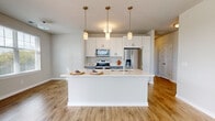 This well-appointed 1-bedroom, 2-bathroom residence at 4301 Yates Dr offers a thoughtfully designed open-concept floor plan with generous living space spread across a single level. The heart of the home is a combined dining, kitchen, and living area that flows seamlessly together. The kitchen is a standout feature, showcasing crisp white shaker cabinetry, two-tone gray lower cabinets, a large center island with a double-basin stainless steel sink, light quartz countertops, and a full suite of stainless steel appliances including a French door refrigerator, electric range, and built-in microwave. Three pendant lights illuminate the island, adding a modern touch. The living area is bathed in natural light from large windows with views of the surrounding neighborhood. Warm wood-look flooring runs throughout the main living spaces, while the spacious bedroom features plush carpeting and a wide window. The primary bathroom includes a vanity with quartz countertops and convenient access to a dedicated walk-in closet with built-in shelving and hanging rods. Four closets in total provide exceptional storage throughout. A dedicated laundry room houses a stacked washer and dryer unit with additional wire shelving. The residence also includes a private balcony, a utility room, and two hallways connecting the well-organized layout.