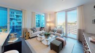 This single-floor residence showcases a thoughtfully designed layout with a contemporary aesthetic throughout. The open-concept living room serves as the centerpiece, bathed in abundant natural light streaming through floor-to-ceiling windows and glass doors that open to a private balcony, offering sweeping urban views. The space is finished with dark hardwood flooring and features floating wall shelves, a textured media console, and access to adjoining rooms.

The kitchen is outfitted with warm wood cabinetry extending to the ceiling, white quartz countertops, a subtle wave-patterned tile backsplash, and stainless steel appliances including a range, dishwasher, and built-in microwave.

The primary bedroom features a dramatic dark accent wall, an upholstered headboard, and a large window that frames city views. Additional bedrooms offer floor-to-ceiling windows, built-in shelving, and dedicated desk areas, providing functional versatility.

The primary bathroom presents a clean, spa-like atmosphere with a dual-sink wood vanity, backlit mirror, and light stone-tile flooring. A second bathroom echoes the same design language with a single vanity and coordinating finishes throughout, maintaining a cohesive, modern character across the entire residence.