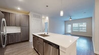 Located at Champions Gate in San Antonio, TX, this well-appointed 2-bedroom, 3-bathroom residence offers a thoughtfully designed single-level layout. The open-concept kitchen and living area serves as the heart of the home, featuring a large center island with a quartz countertop, undermount sink, and stylish pendant lighting. Dark-toned cabinetry with brushed nickel hardware pairs with a subway tile backsplash, and a full suite of stainless steel appliances—including a refrigerator, range, microwave, and dishwasher—completes the kitchen. Wood-look flooring flows through the main living areas, while a ceiling fan adds comfort to the bright, open living room, which benefits from natural light through large windows and access to an exterior door. Both bedrooms are carpeted and include ceiling fans and windows that bring in natural light. The primary bedroom connects to an en-suite bathroom featuring dual sinks with quartz countertops, dark cabinetry, wood-look flooring, and a glass-enclosed walk-in shower. A second full bathroom mirrors the same refined finishes. Two closets provide ample storage. The space combines modern design elements with practical functionality throughout.