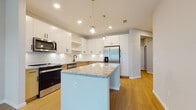 Located at 1650 Clearwater Largo Rd in Largo, Florida, this single-floor residence offers a clean, modern design with a bright and open layout. Light wood flooring flows seamlessly throughout the space, contributing to a warm and cohesive aesthetic.

The kitchen serves as the centerpiece of the home, outfitted with a full suite of stainless steel appliances including a refrigerator with ice and water dispenser, range, microwave, and dishwasher. A large central island with granite countertops provides generous prep and seating space, while a mix of upper white shaker cabinets and lower natural wood cabinetry creates a stylish two-tone contrast. Pendant globe lighting and recessed ceiling lights illuminate the space effectively. A white subway tile backsplash adds a classic finishing touch.

The living area is airy and welcoming, featuring a ceiling fan, a glass-paneled door, and multiple windows fitted with white horizontal blinds that allow for natural light and outdoor views of the surrounding greenery. Additional bedroom spaces benefit from large windows that carry in plentiful natural light.

The bathroom is well-appointed with a granite-topped vanity with an undermount sink, a full soaking tub with shower combination, and clean white tile surround. The overall design of this residence emphasizes contemporary finishes, functional layouts, and a light, neutral palette throughout.