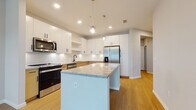 Located at 1650 Clearwater Largo Rd in Largo, Florida, this single-floor residence offers a clean, modern design with a bright and open layout. Light wood flooring flows seamlessly throughout the space, contributing to a warm and cohesive aesthetic.

The kitchen serves as the centerpiece of the home, outfitted with a full suite of stainless steel appliances including a refrigerator with ice and water dispenser, range, microwave, and dishwasher. A large central island with granite countertops provides generous prep and seating space, while a mix of upper white shaker cabinets and lower natural wood cabinetry creates a stylish two-tone contrast. Pendant globe lighting and recessed ceiling lights illuminate the space effectively. A white subway tile backsplash adds a classic finishing touch.

The living area is airy and welcoming, featuring a ceiling fan, a glass-paneled door, and multiple windows fitted with white horizontal blinds that allow for natural light and outdoor views of the surrounding greenery. Additional bedroom spaces benefit from large windows that carry in plentiful natural light.

The bathroom is well-appointed with a granite-topped vanity with an undermount sink, a full soaking tub with shower combination, and clean white tile surround. The overall design of this residence emphasizes contemporary finishes, functional layouts, and a light, neutral palette throughout.