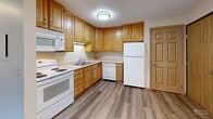 This 2-bedroom, 1-bathroom unit in Sioux Falls, South Dakota offers a practical and well-organized single-floor layout designed for comfortable everyday living. The combined kitchen and living area forms the heart of the home, with the kitchen showcasing warm oak cabinetry, ample upper and lower storage, light countertops, and a full suite of white appliances including a range, microwave, dishwasher, and refrigerator. The kitchen flows onto durable wood-look luxury vinyl plank flooring, which also extends into the living area. A sliding glass door in the living space fills the room with natural light and provides outdoor views, while a wall-mounted AC unit ensures year-round comfort. Both bedrooms feature plush wall-to-wall carpeting, ceiling fans with light fixtures, baseboard heating, and windows that let in natural light. The primary bedroom offers generous closet space with multiple sliding and double-door wood closets. The full bathroom is finished with tile flooring, a tub-shower combination, a wooden vanity with a white countertop, and a mirrored medicine cabinet. Neutral warm tones and textured ceilings carry throughout, giving the space a cohesive and understated character.
