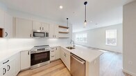 Located at 770 Water Street in Framingham, MA, this thoughtfully designed 3-bedroom, 2-bathroom residence offers a clean, modern aesthetic across a well-organized single-floor layout. Light hardwood flooring flows seamlessly throughout, complementing the bright, neutral color palette that defines the space.

The open-concept kitchen and living area serves as the heart of the home. The kitchen is outfitted with crisp white cabinetry, a classic subway tile backsplash, quartz countertops, and a peninsula with an integrated sink — ideal for both cooking and casual dining. Stainless steel appliances and stylish pendant lighting add a polished, contemporary feel, while open wooden shelving provides both function and visual warmth.

The living area extends naturally from the kitchen, bathed in natural light from large windows that frame outdoor views of the surrounding landscape. Each of the three bedrooms continues the clean, airy aesthetic, with hardwood floors, recessed lighting, and generous windows. The spacious primary bedroom is notably well-sized and includes a dedicated closet with built-in shelving.

Both bathrooms are finished with hexagonal tile flooring, soft blue-gray walls, and white subway tile shower surrounds. The primary bath features a glass-enclosed walk-in shower and a warm wood vanity, while the second bath offers a full tub-shower combination.
