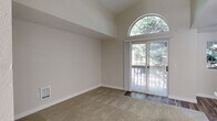 Located in Edmonds, WA, this one-bedroom, one-bathroom unit offers a thoughtfully designed layout that maximizes its compact footprint. The living area is a standout, featuring soaring vaulted ceilings and a striking arched window positioned above sliding glass doors that open to a private balcony. The wooded views framed by the balcony and the abundant natural light create an airy, open atmosphere throughout the main living space, which transitions from plush carpet to hardwood-style flooring near the entry.

The kitchen is efficiently arranged in a galley style, outfitted with warm medium-toned wood cabinetry, light stone-look countertops, a stainless steel double-basin sink with a modern faucet, and black and stainless steel appliances including a refrigerator, range, microwave, and dishwasher. Durable wood-look flooring runs throughout the kitchen, adding a cohesive, contemporary feel.

The bedroom is a comfortable, well-proportioned space with soft carpet and neutral walls. It is accompanied by a dedicated closet with built-in shelving and hanging rods, offering practical storage. The full bathroom features a tub-shower combination with clean white surrounds. A hallway connects the rooms, completing this well-organized and functional single-level residence.