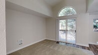 Located in Edmonds, WA, this one-bedroom, one-bathroom unit offers a thoughtfully designed layout that maximizes its compact footprint. The living area is a standout, featuring soaring vaulted ceilings and a striking arched window positioned above sliding glass doors that open to a private balcony. The wooded views framed by the balcony and the abundant natural light create an airy, open atmosphere throughout the main living space, which transitions from plush carpet to hardwood-style flooring near the entry.

The kitchen is efficiently arranged in a galley style, outfitted with warm medium-toned wood cabinetry, light stone-look countertops, a stainless steel double-basin sink with a modern faucet, and black and stainless steel appliances including a refrigerator, range, microwave, and dishwasher. Durable wood-look flooring runs throughout the kitchen, adding a cohesive, contemporary feel.

The bedroom is a comfortable, well-proportioned space with soft carpet and neutral walls. It is accompanied by a dedicated closet with built-in shelving and hanging rods, offering practical storage. The full bathroom features a tub-shower combination with clean white surrounds. A hallway connects the rooms, completing this well-organized and functional single-level residence.