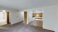 This single-floor, 2-bedroom, 1-bathroom residence offers a practical and comfortable layout designed for efficient everyday living. The open living area features neutral-toned carpet underfoot and clean white walls, creating a bright and versatile space that accommodates a variety of furniture arrangements. A textured ceiling adds subtle character throughout.

The kitchen is positioned adjacent to the living area and is defined by warm oak cabinetry, a decorative tile backsplash, and a double-basin sink. A peninsula with a laminate countertop provides a natural divider between the kitchen and living space, offering additional prep area and casual seating potential. The kitchen also features a white dishwasher and recessed lighting, contributing to a clean and functional cooking environment.

A doorway visible from the main living area leads to the private sleeping quarters and bathroom, ensuring a clear separation between communal and private spaces. The layout flows logically, making efficient use of the available square footage. Neutral finishes and consistent trim work throughout give the space a cohesive, move-in-ready appearance. This residence is well-suited for those seeking a straightforward, no-frills layout with all essential amenities on a single, accessible level.