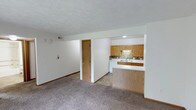 This single-floor, 2-bedroom, 1-bathroom residence offers a practical and comfortable layout designed for efficient everyday living. The open living area features neutral-toned carpet underfoot and clean white walls, creating a bright and versatile space that accommodates a variety of furniture arrangements. A textured ceiling adds subtle character throughout.

The kitchen is positioned adjacent to the living area and is defined by warm oak cabinetry, a decorative tile backsplash, and a double-basin sink. A peninsula with a laminate countertop provides a natural divider between the kitchen and living space, offering additional prep area and casual seating potential. The kitchen also features a white dishwasher and recessed lighting, contributing to a clean and functional cooking environment.

A doorway visible from the main living area leads to the private sleeping quarters and bathroom, ensuring a clear separation between communal and private spaces. The layout flows logically, making efficient use of the available square footage. Neutral finishes and consistent trim work throughout give the space a cohesive, move-in-ready appearance. This residence is well-suited for those seeking a straightforward, no-frills layout with all essential amenities on a single, accessible level.