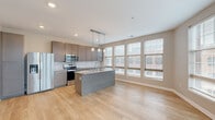 Located at 820 E Long Street in Columbus, Ohio, this well-appointed 2-bedroom, 2-bathroom residence offers a thoughtfully designed single-floor layout. The open-concept kitchen and living area serves as the heart of the home, highlighted by a large center island with granite countertops, pendant lighting, and a full suite of stainless steel appliances including a French door refrigerator, electric range, and over-the-range microwave. Warm-toned hardwood-style flooring flows throughout the main living areas, complemented by a white subway tile backsplash and rich, gray-toned cabinetry. A wall of oversized windows floods the living room with natural light and provides views of the surrounding Columbus cityscape. Both bedrooms feature plush carpet and generous closet space, with the primary bedroom boasting a dedicated walk-in closet with wire shelving systems. Each bathroom is finished with granite-topped vanities, dark wood cabinetry, and glass-enclosed showers. Clean, neutral wall tones and recessed lighting throughout create a bright and cohesive atmosphere. A well-proportioned hallway connects the living areas to the private sleeping quarters, enhancing the overall sense of flow and functionality within the home.
