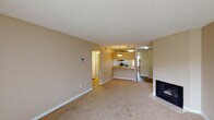 This single-floor residence is thoughtfully arranged to maximize functionality and comfort. The living area serves as the central gathering space, finished with plush wall-to-wall carpet and warm beige walls that create an inviting atmosphere. A fireplace with a tiled hearth anchors one end of the room, while a nearby closet provides convenient storage. The open layout connects seamlessly to the kitchen via a raised peninsula counter, making the space well-suited for everyday living and entertaining.

The kitchen features medium-toned wood cabinetry, granite-look countertops, hardwood-style flooring, and black appliances including a range and a stainless steel refrigerator. A window above the sink brings natural light into the space. A textured ceiling is present throughout the unit, adding subtle dimension overhead.

The two bedrooms are each carpeted and finished in the same neutral palette. Both include closets—one with bifold doors and another with a sliding door—offering ample storage. A window in one bedroom allows natural light to filter in.

Two full bathrooms serve the unit, each equipped with a tub-shower combination, wood-toned vanity cabinetry, granite-look countertops, and hardwood-style flooring, providing a cohesive and practical finish throughout.