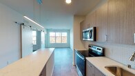 This single-floor residence presents a thoughtfully designed layout with a contemporary aesthetic throughout. The kitchen is a functional centerpiece, outfitted with a full suite of stainless steel appliances including an electric range, over-the-range microwave, refrigerator, and dishwasher. Light wood-toned cabinetry extends to the ceiling, providing ample storage, while white quartz countertops and a subway tile backsplash contribute a clean, modern finish. Pendant lighting and recessed fixtures illuminate the space effectively.

The open-concept living and dining area flows naturally from the kitchen, featuring neutral-toned luxury vinyl tile flooring and a large picture window that brings in generous natural light and offers views of a wooded outdoor landscape. A sliding barn door adds a distinctive architectural detail, providing flexible room division. A separate bedroom features carpeted flooring and a horizontal band of windows positioned high on the wall, allowing light while maintaining privacy. Additional bedrooms include standard windows and vinyl tile flooring. The bathroom is finished with tile flooring and includes a walk-in glass-enclosed shower with brushed nickel hardware and fixtures. The overall design is clean, neutral, and move-in ready.