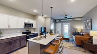 This well-designed 2-bedroom, 2-bathroom unit offers a thoughtful single-floor layout that maximizes functionality. The open-concept living and kitchen area serves as the heart of the unit, where a large center island with a quartz countertop and bar seating anchors the space. Pendant lighting hangs above the island, complementing the stainless steel appliances, two-tone cabinetry featuring white upper cabinets and dark lower cabinets, and light wood-style flooring. The living area connects seamlessly to the kitchen and features a ceiling fan, exposed silver ductwork that lends an industrial character, and a glass-panel door that brings in natural light.

Both bedrooms are carpeted and finished with neutral tones, offering a calm and comfortable atmosphere. The bathrooms are clean and functional, featuring walk-in showers with matte black fixtures and light wood-style flooring. Three closets provide ample storage throughout the unit. A dedicated laundry area houses a stacked washer and dryer, adding everyday convenience. The consistent use of gray walls, black hardware, and modern fixtures throughout creates a cohesive, contemporary aesthetic.