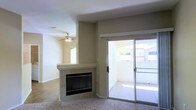 This single-floor residence offers a well-designed open layout that maximizes both comfort and functionality. The main living area is a welcoming space anchored by a corner fireplace with a granite-style surround, providing a natural focal point for the room. Neutral-toned walls and light carpet flooring create a clean, versatile backdrop throughout the space. A ceiling fan overhead contributes to year-round comfort while adding a practical architectural detail to the living area. Natural light flows generously into the interior through multiple windows and a large sliding glass door, which opens directly onto a private outdoor patio. The patio extends the living space outdoors, offering views of surrounding greenery and neighboring structures. The transition between indoor and outdoor areas is seamless, making the patio a natural extension of the interior. The open flow between spaces enhances the sense of roominess throughout. Overall, the residence presents a straightforward and functional design, with thoughtful touches such as the fireplace and abundant natural light contributing to a comfortable and inviting ambiance suited for everyday living.