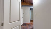 Located on East Franklin Street in Richmond, VA, this one-bedroom, one-bathroom unit blends historic industrial character with functional modern living. The space is defined by striking exposed brick walls, rich original hardwood floors with deep, warm tones, and overhead wood beam ceilings complemented by visible metal ductwork — all hallmarks of a thoughtfully preserved historic conversion.

The combined kitchen and living area forms the heart of the unit. The kitchen is well-equipped with rich cherry wood cabinetry, dark granite countertops, stainless steel appliances including a range and dishwasher, and a layout that maximizes efficiency. Exposed brick forms a dramatic backdrop along one wall, reinforcing the industrial-loft aesthetic throughout.

The bedroom offers a cozy yet characterful retreat, featuring the same handsome hardwood floors, a rustic barn-style door with aged patina, and multiple windows that invite natural light and outdoor views of the surrounding neighborhood.

The bathroom is clean and functional, finished with tile flooring, a tub-shower combination, and cherry wood vanity cabinetry consistent with the rest of the unit's design palette.

Throughout the space, the interplay of raw historic materials and modern finishes creates a warm, urban ambiance well-suited to Richmond's vibrant East End neighborhood.