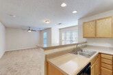 Located at 5034 Hilltop Rd in Greensboro, NC, this single-floor, one-bedroom, one-bathroom residence offers a well-organized layout across a comfortable footprint. The open-concept kitchen flows directly into the living room via a peninsula counter, creating a connected and functional common area. The kitchen features light oak cabinetry, light-toned countertops, a double stainless steel sink, and black appliances including a range, over-the-range microwave, refrigerator, and dishwasher. Wood-look flooring grounds the kitchen space. The living room is carpeted and benefits from abundant natural light through large windows fitted with horizontal blinds. A ceiling fan overhead adds comfort and airflow to the space. The bedroom is generously sized with plush carpet flooring, a ceiling fan with light fixture, and a window that brings in natural light. A closet provides dedicated storage. The bathroom features warm hardwood-style flooring, an oak vanity with a mirror and lighted fixture, a tall storage cabinet, and a shower-tub combination. A utility room rounds out the layout, adding practical storage and functional space. Textured ceilings are consistent throughout the home.