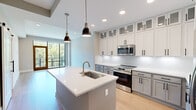 Located at 350 Carraway Crossing in Chapel Hill, NC, this thoughtfully designed one-bedroom, two-bathroom residence offers a contemporary open-concept layout with high-end finishes throughout. The gourmet kitchen is a standout feature, showcasing two-tone shaker cabinetry extending to the ceiling with glass-front upper panels, quartz countertops, stainless steel appliances, a deep undermount sink, and a central island with pendant lighting — all seamlessly connected to the living area. Light hardwood flooring flows through the main living spaces, while floor-to-ceiling windows and sliding glass doors flood the interior with natural light and provide lush, tree-lined views. The living room opens to a private balcony, enhancing the connection to the outdoors. The bedroom features plush carpeting and an expansive window wall overlooking the surrounding greenery. The primary bathroom is appointed with large-format marble-style tile, a frameless glass walk-in shower complete with a built-in bench and dual showerhead, and a vanity with stone countertops. A dedicated closet and a second full bathroom add practical convenience. The entrance and hallway provide a clean, welcoming transition into the home, completing this polished and functional residence.