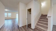 This two-story home offers a thoughtfully designed layout with consistent, modern finishes throughout. The kitchen serves as a functional centerpiece, featuring white shaker-style cabinetry, granite countertops, a central island with a sink, and a full suite of stainless steel appliances including a refrigerator with ice and water dispenser, electric range, and microwave. Wood-look vinyl plank flooring runs throughout the main living areas, lending warmth and continuity to the open-concept lower level. A convenient storage closet is tucked beneath the carpeted staircase, maximizing utility in the entryway area. The upper floor is home to generously sized bedrooms with plush carpeting, including one room featuring a spacious walk-in closet outfitted with dual hanging rods for ample storage. The bathrooms are finished in a clean, bright aesthetic, with one featuring a wide vanity with white cabinetry, a large mirror, and a tub-shower combination, while a second bathroom offers a similarly streamlined design. Natural light filters in through window treatments, contributing to the home's bright and airy atmosphere. The overall ambiance is clean, neutral, and move-in ready, providing a versatile canvas suited to a variety of interior styles.