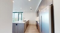 This modern 2-bedroom, 2-bathroom residence offers a thoughtfully designed open-concept layout with contemporary finishes throughout. The combined kitchen and living area serves as the heart of the home, highlighted by dramatic floor-to-ceiling windows that frame sweeping panoramic city views and flood the space with natural light. A sliding glass door opens to a balcony, extending the living area outdoors. Light hardwood flooring flows seamlessly throughout the main living spaces and bedrooms, complementing the clean, neutral palette.

The kitchen is well-appointed with flat-front wood-toned cabinetry reaching to the ceiling, stainless steel appliances including a refrigerator, range, and over-the-range microwave, a marble-style tile backsplash, and a large island with a white quartz countertop and an integrated sink — ideal for both cooking and casual dining.

The spacious primary bedroom features an entire wall of floor-to-ceiling windows showcasing city skyline views, along with a dedicated walk-in closet outfitted with built-in shelving. The second bedroom is equally bright with its own large window. Both bathrooms are finished with large-format tile flooring, floating wood-toned vanities, white quartz countertops, and wall-mounted cabinetry, delivering a clean, modern aesthetic.