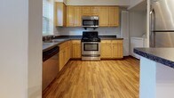 Located at 779 Queens Ct in Charlottesville, Virginia, this single-floor residence offers a well-organized and functional layout throughout. The kitchen is a practical centerpiece, outfitted with light wood cabinetry, dark granite-style countertops, and stainless steel appliances including a refrigerator, electric range, microwave, and dishwasher. Warm hardwood-style flooring runs through the kitchen and main living areas, adding a consistent, clean aesthetic. A pass-through opening connects the kitchen to the adjacent living space, enhancing the open feel of the floor plan. The living area features crown molding and hardwood-style flooring, with a window providing natural light. Multiple bedrooms are finished with plush carpeting, crown molding, and windows fitted with blinds that frame views of the surrounding greenery. The bathroom includes a full tub-shower combination with chrome fixtures and a clean, bright finish. A dedicated laundry area with a full-size washer and dryer is conveniently located within the unit. Throughout the home, the consistent use of white walls, crown molding, and natural light creates a bright and tidy atmosphere well-suited for comfortable everyday living.